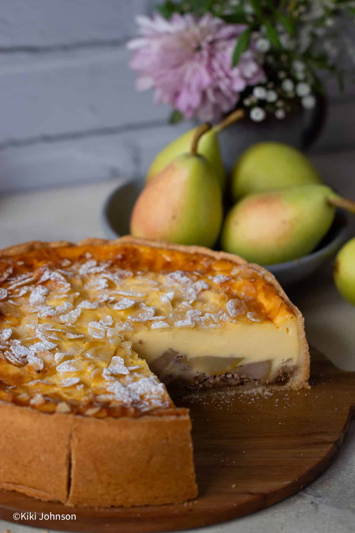 ein angeschnittener Birnenkuchen mit frischen Birnen bedeckt von Vanillepudding Schicht und Mandelblättchen