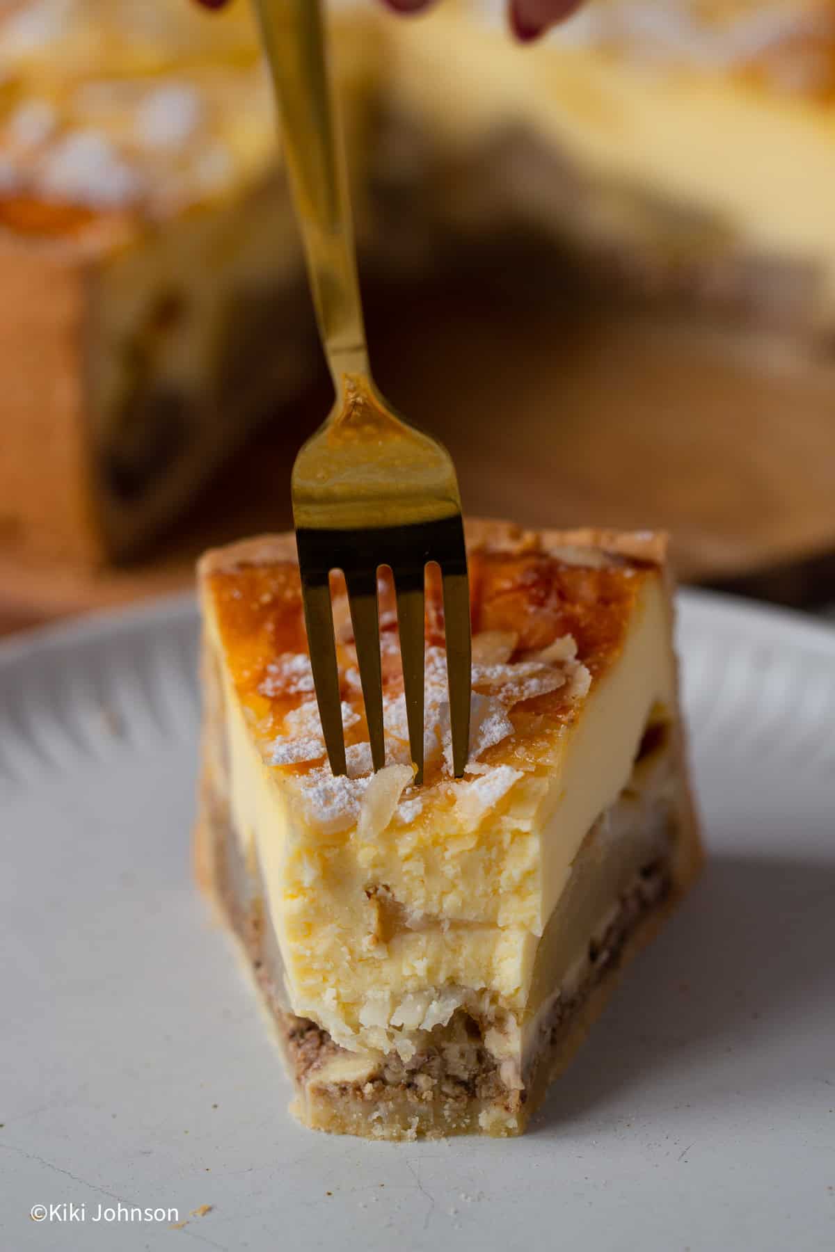 eine Gabel sticht in ein Stück Birnenkuchen mit Vanillepudding Schmand Guss und Mandelblättchen dekoriert