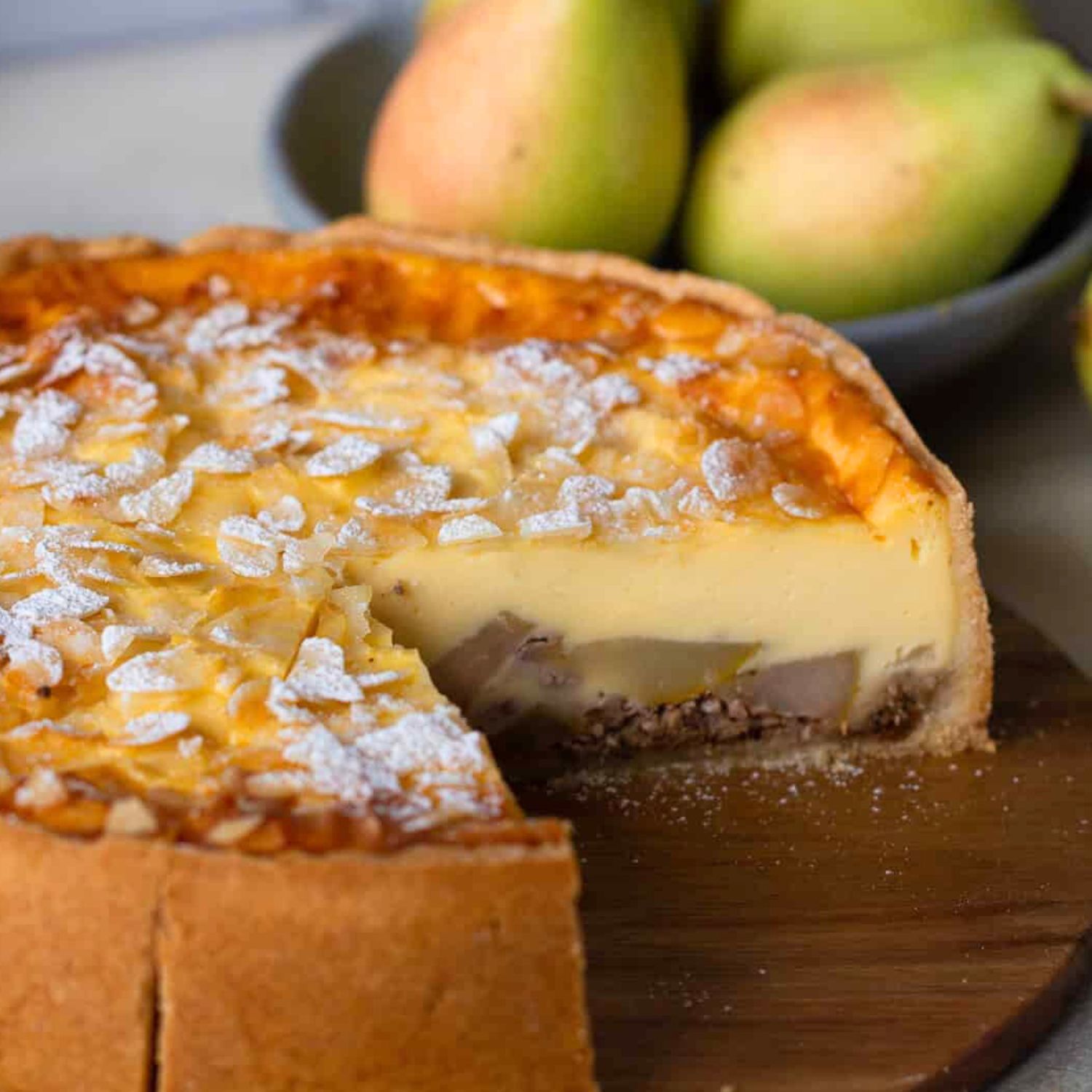 ein angeschnittener Birnenkuchen mit Pudding und frischen Birnen mit Mandelblättchen verziert