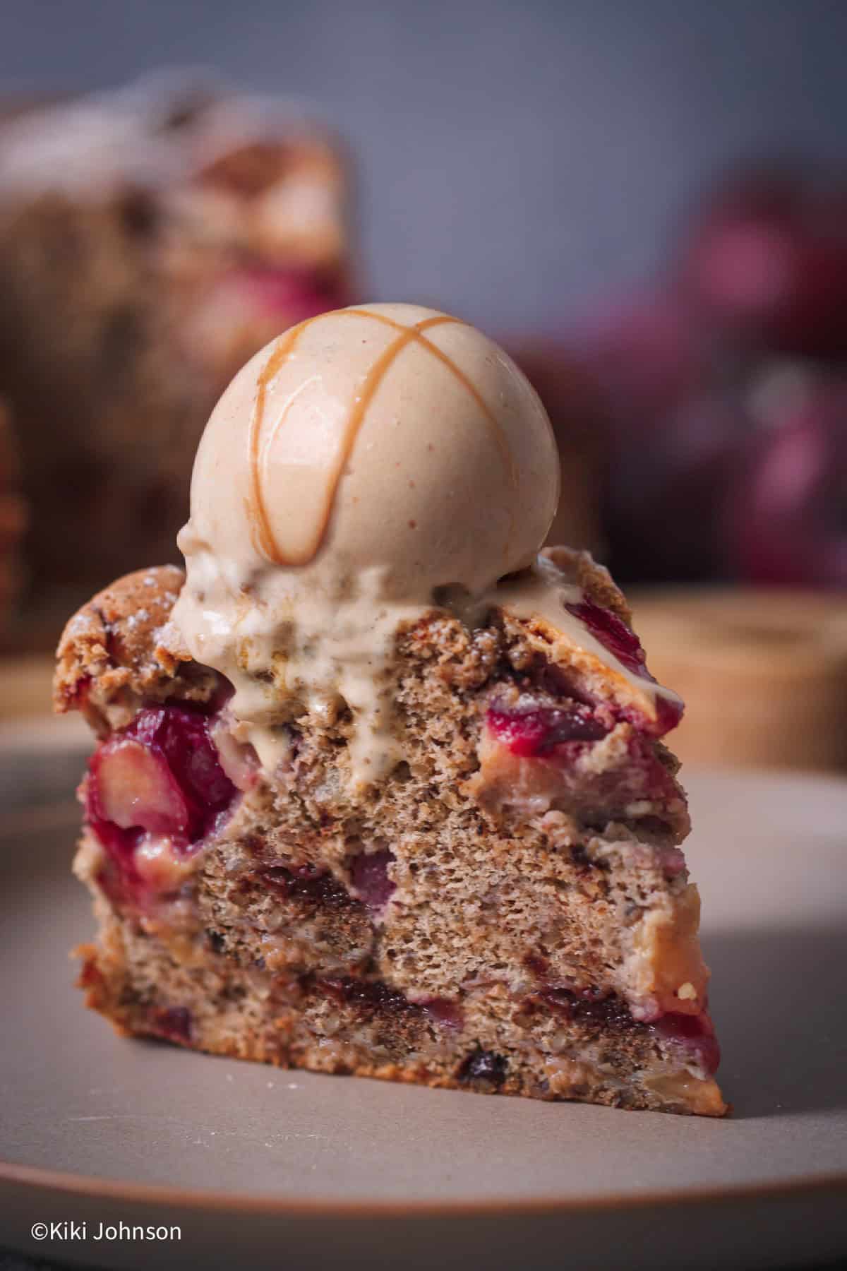 a slice of walnut cake with chocolate chips and plum chunks topped with. a scoop of walnut caramel ice cream 