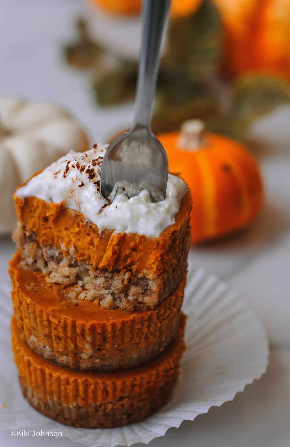 eine Gabel sticht in drei gestapelte Kürbis Cupcakes mit Spekulatius-Haselnuss Kekskrümel Boden und cremiger Pumpkin-Spice-Füllung auf einem kleinen Dessertteller.