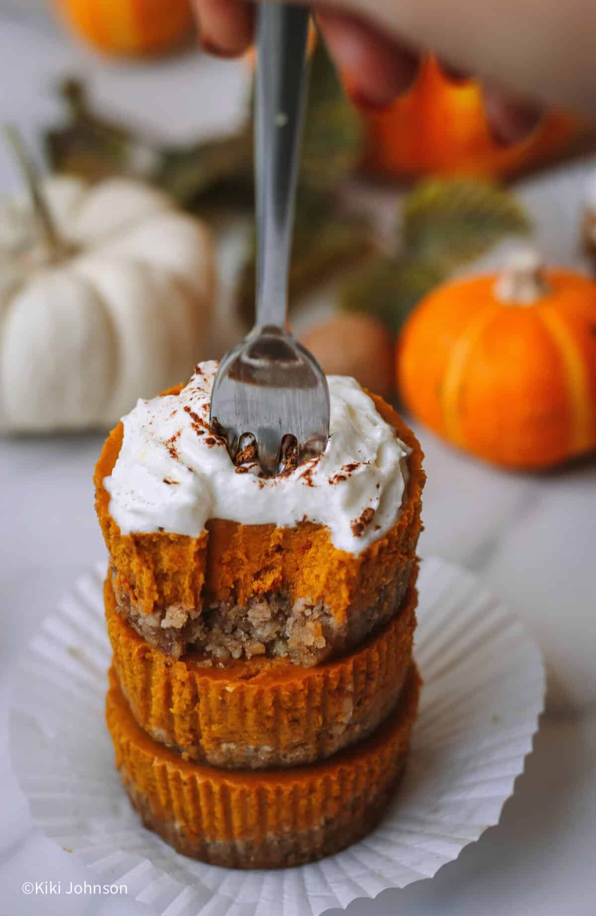 eine Gabel sticht in drei Kürbis Cupcakes mit Spekulatius-Haselnuss-Boden und cremiger Pumpkin-Spice-Füllung auf einem kleinen Dessertteller.