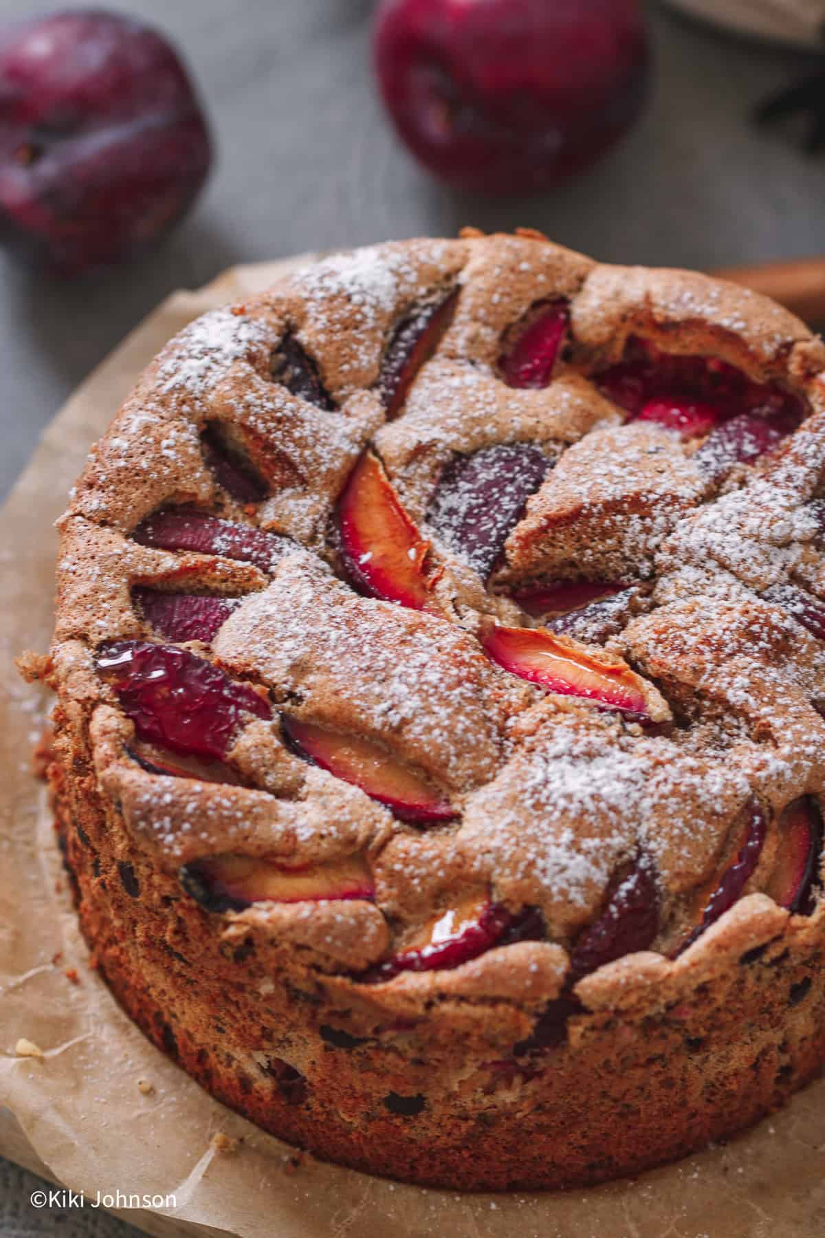 a ground walnut and plum cake on a sheet of baking paper decorated with icing sugar 