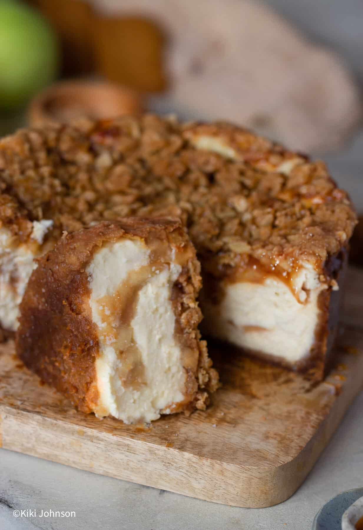 ein angeschnittener Apfel Käsekuchen mit Streusel auf einem Holzbrett 