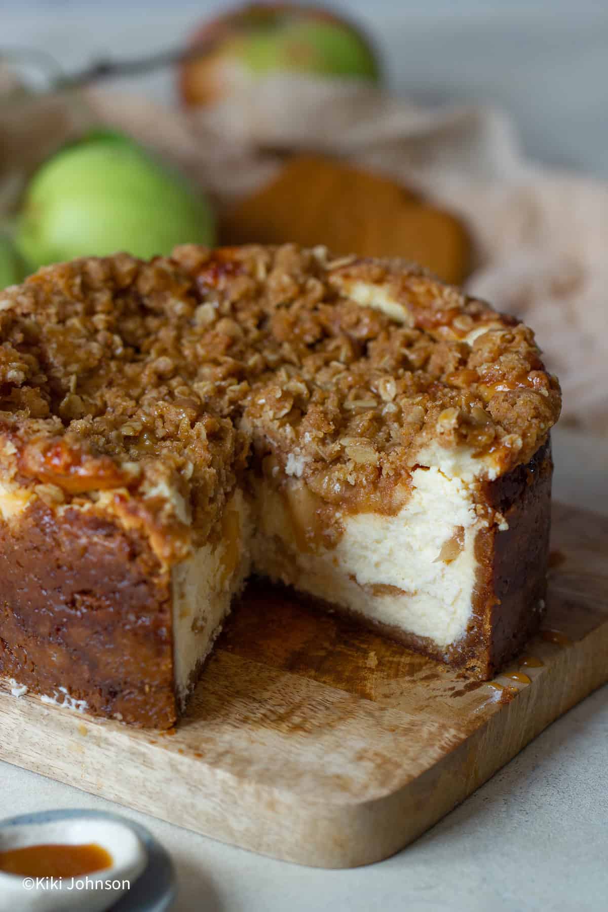 angeschnittener Apfel Käsekuchen mit Streusel und Lotus Keksboden auf einem Holzbrett 