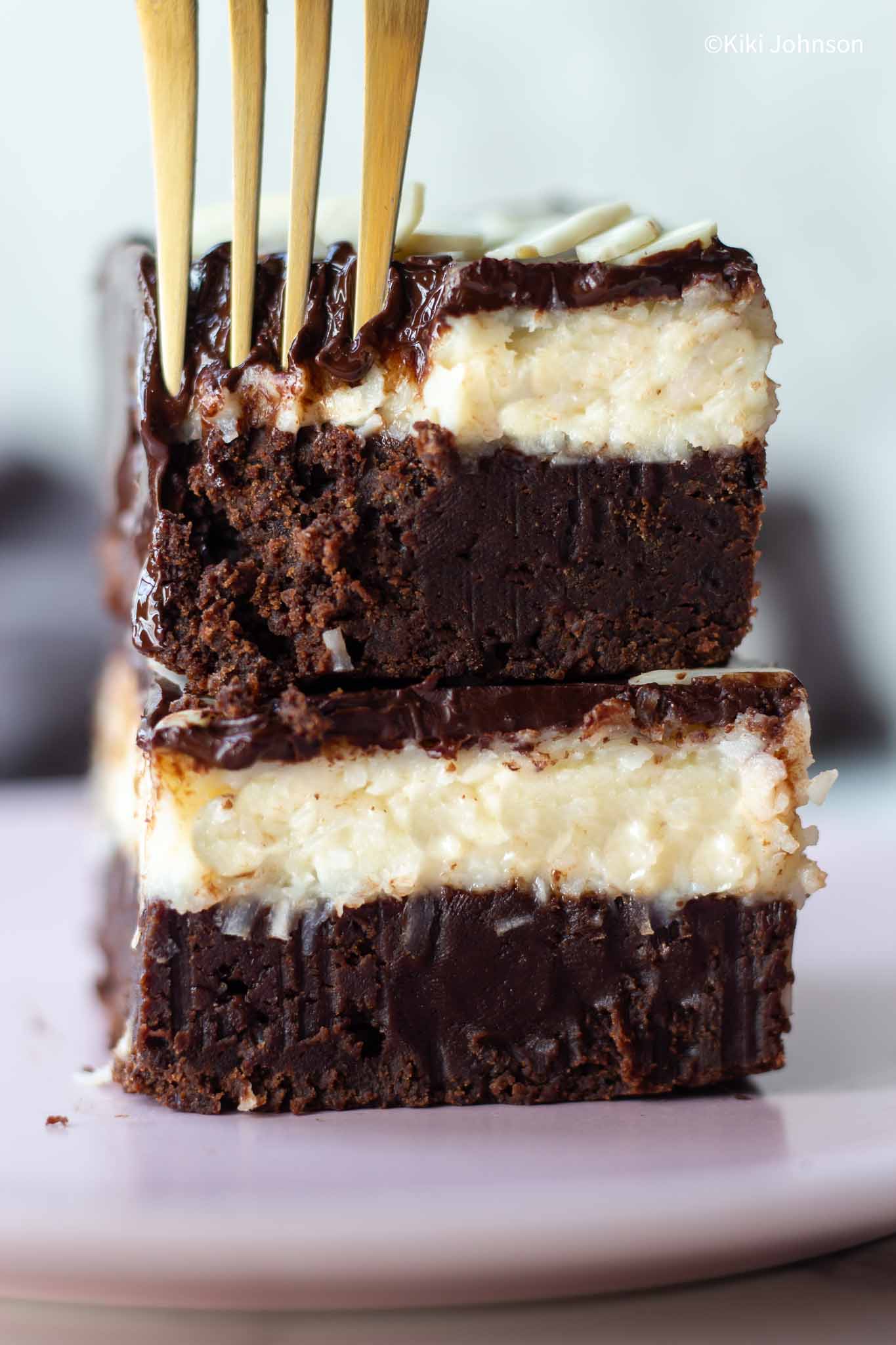 a stack of two fudge brownies with coconut and chocolate ganache with a golden fork