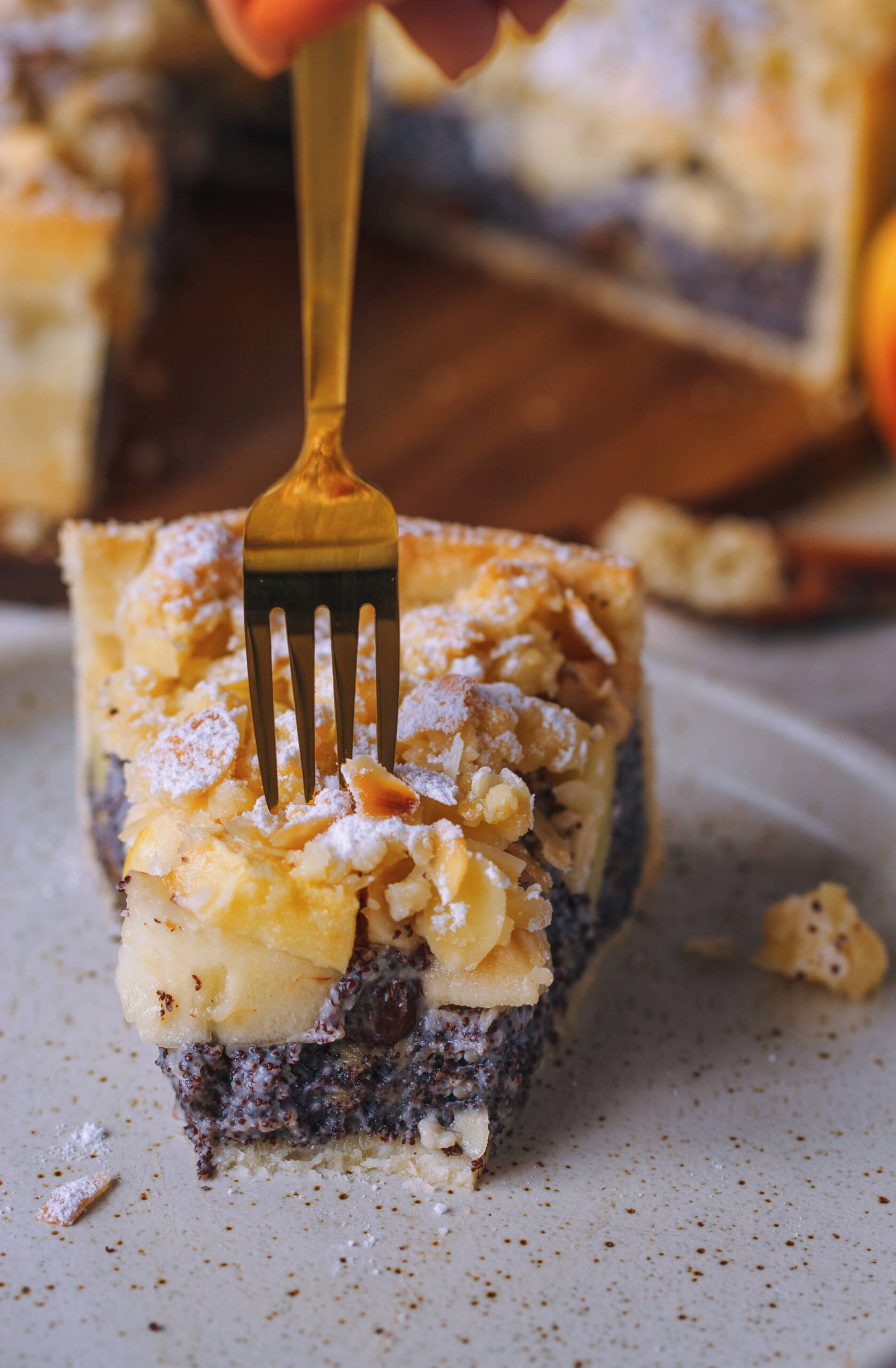 eine Gabel sticht in ein Stück Mohnkuchen mit Äpfeln und Mandel Streuseln
