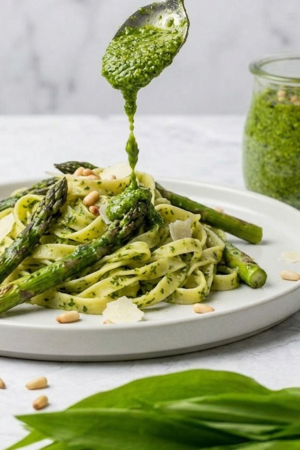 ein TL Bärlauch Pesto wird über einen Teller mit Pesto Bandnudeln mit grünem Spargel gegeben 