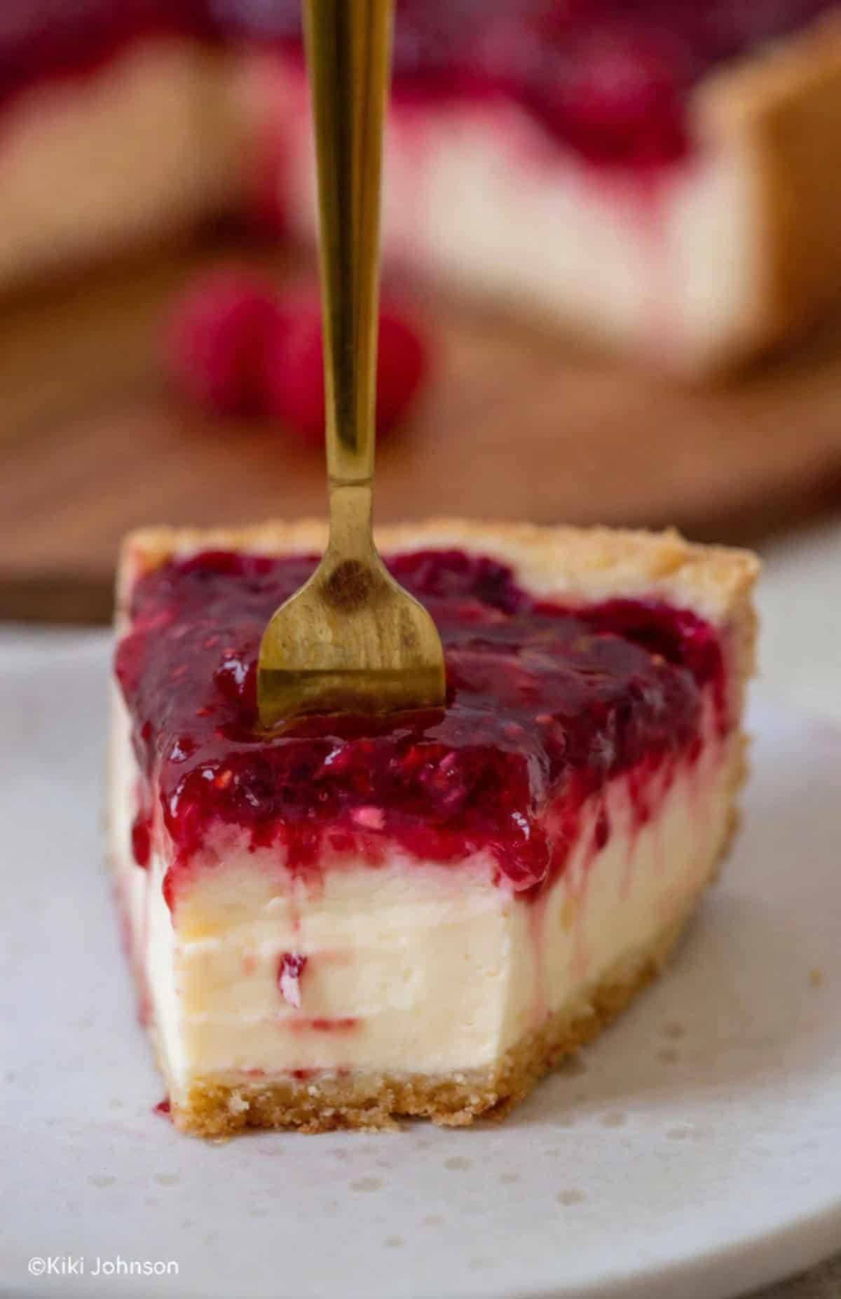 ein halb aufgegessenes Stück Himbeer Pudding Kuchen mit Schmand mit einer goldenen Gabel die in den Kuchen sticht.