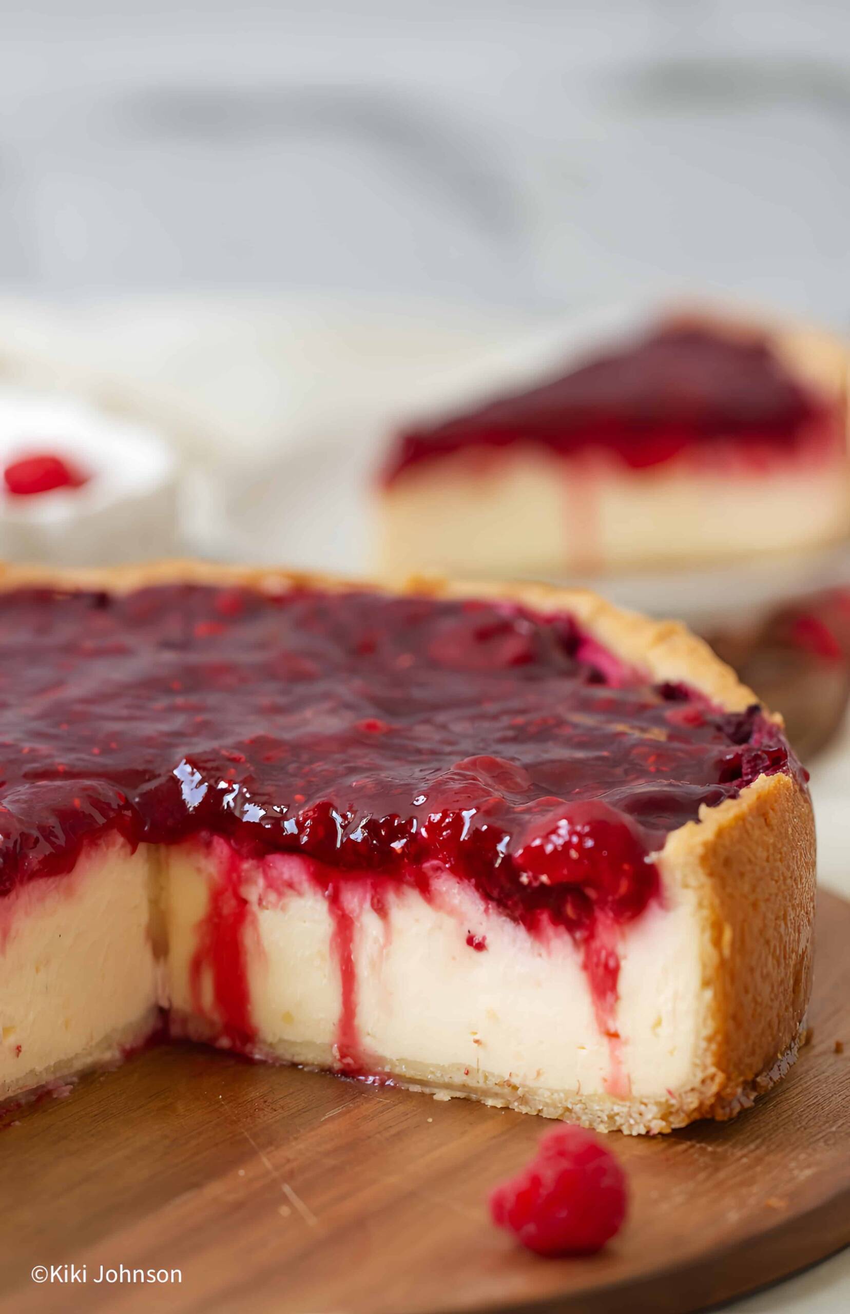 ein angeschnittener Himbeer Schmand Kuchen aif einer Holzplatte