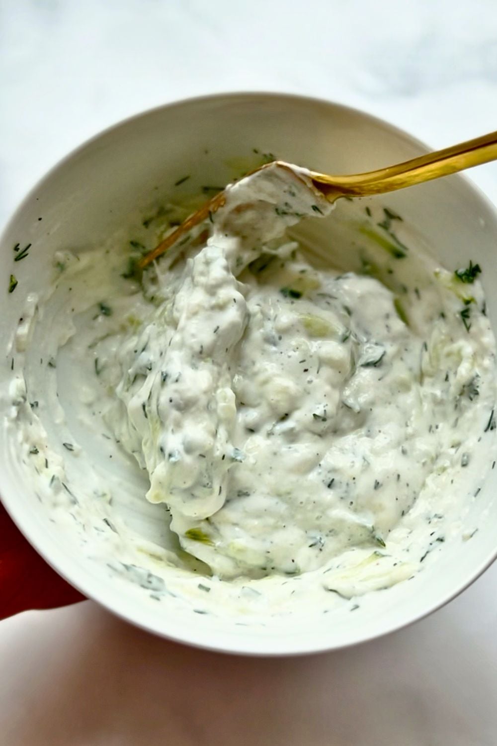tzatziki being mixed in a white bowl 