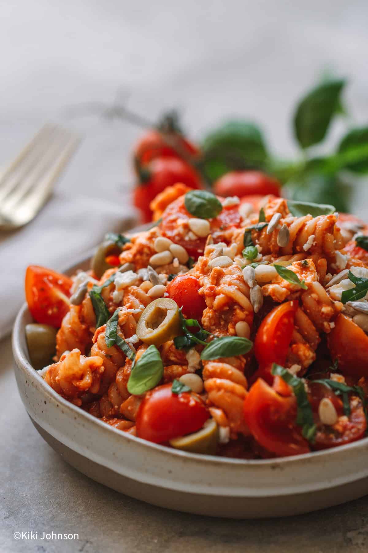 Nudelsalat mit Pesto, Feta, Tomaten und Oliven in einer weissen Schale mit Sonnenblumenkernen dekoriert