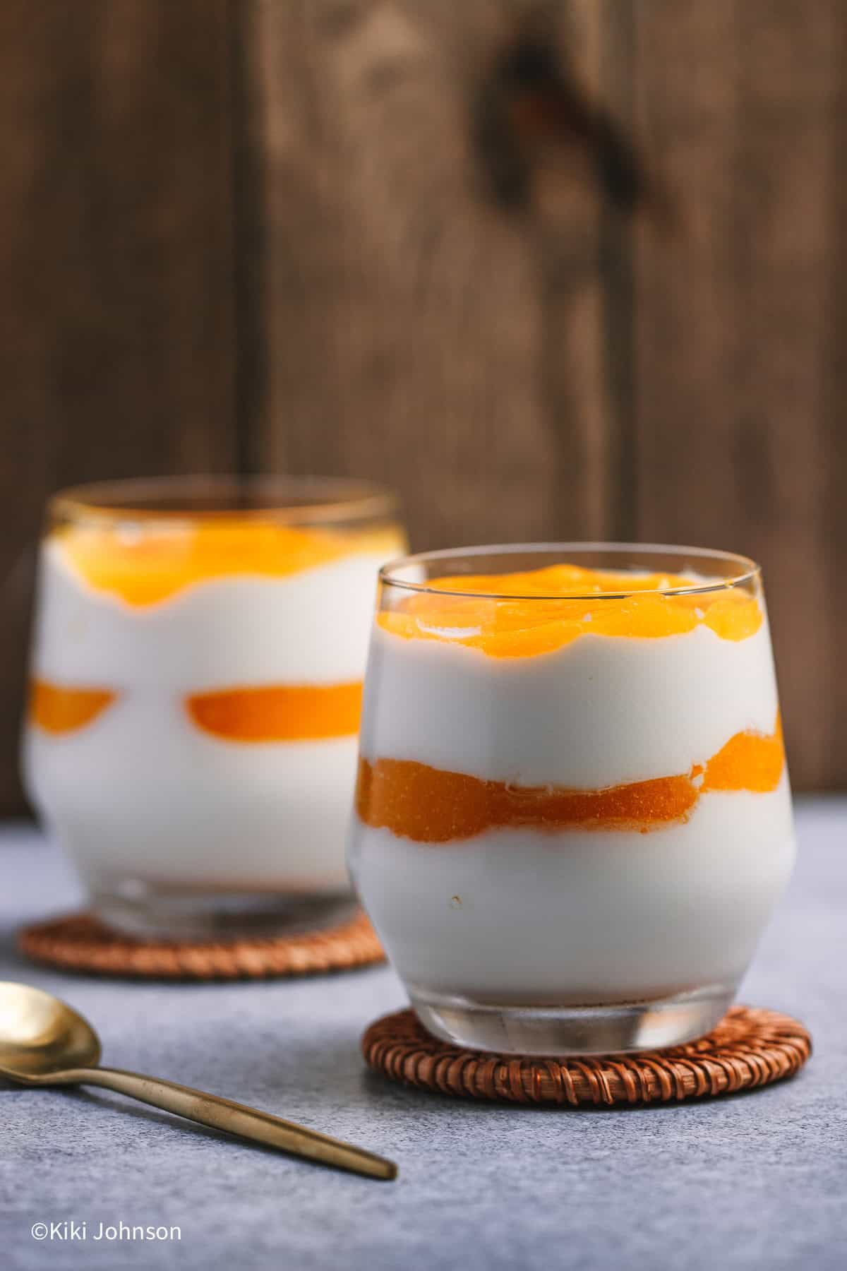2 Gläser mit solero dessert im glas mit joghurt creme und maracuja sosse vor einem hölzernen Hintergrund