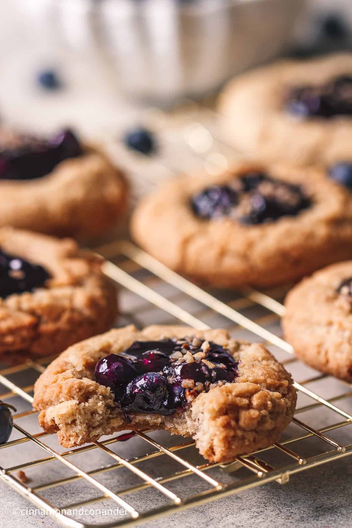 close up of a half eaten blueberry pie cookie with blueberry jam filling on a golden rack 