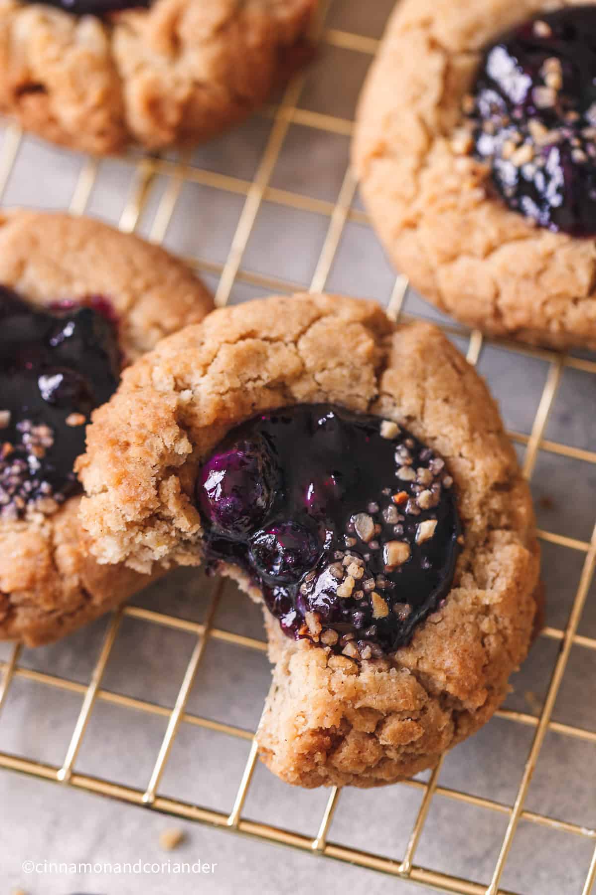 Nahaufnahme von einem angebissenen Blaubeer Cookie mit Blaubeermarmelade in der Mitte auf einem goldenen Gitter 