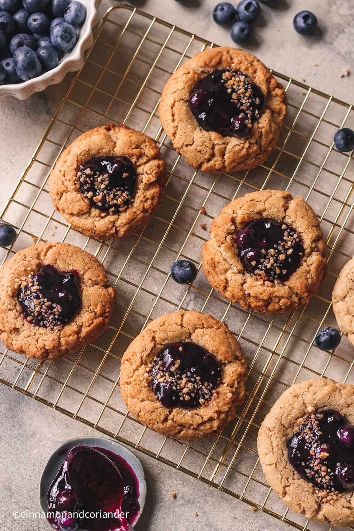 blueberry pie cookies with blueberry jam filling on a golden rack with fresh blueberries in a bowl in the background