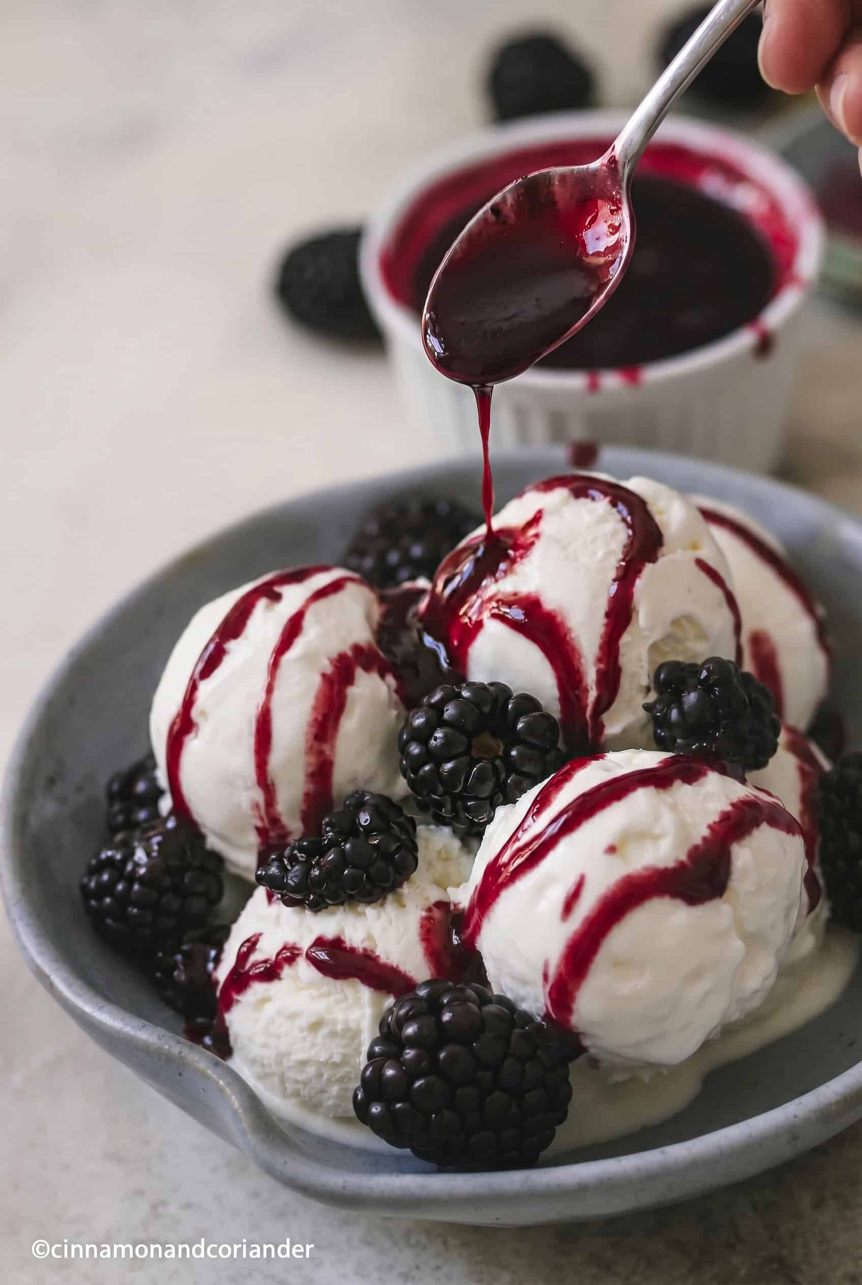 süße Brombeersauce wird über 4 Eiskugeln geträufelt in einem Eisbecher mit frischen Brombeeren