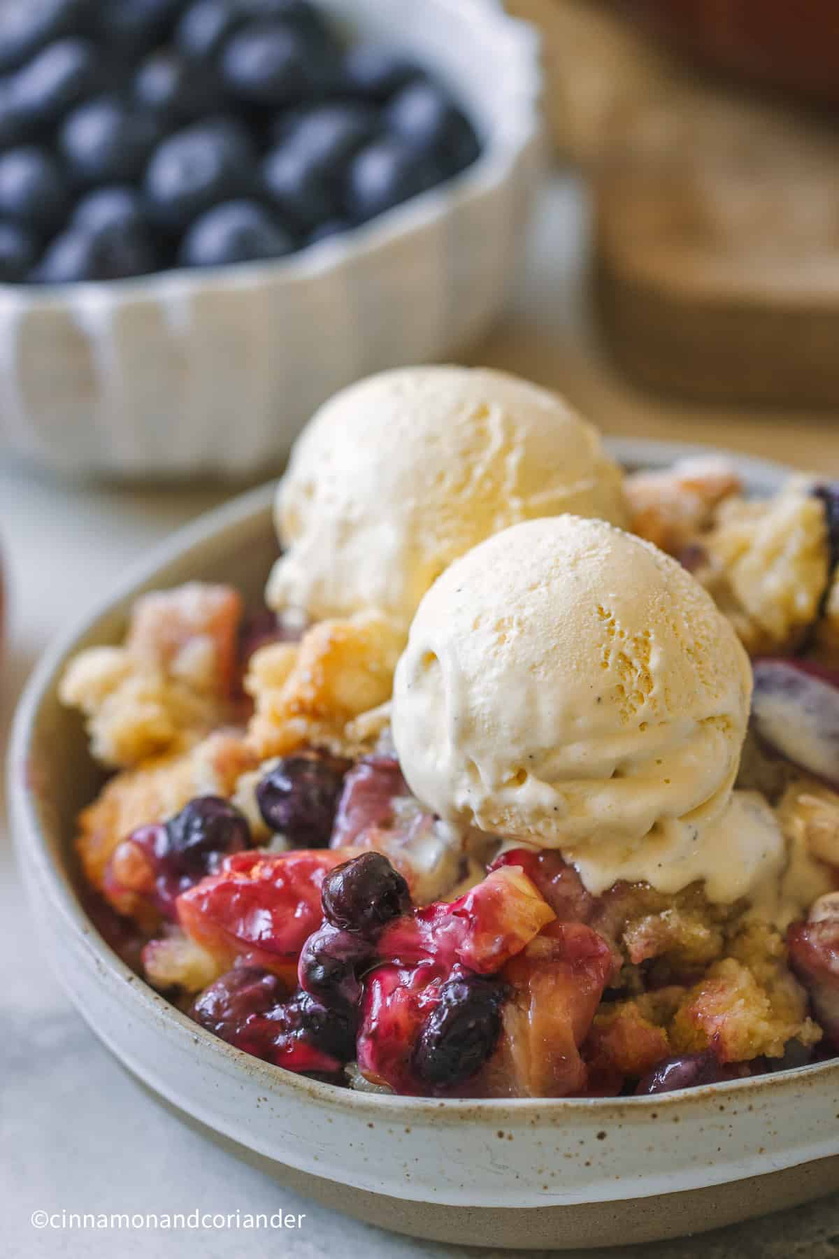 eine Schale mit Pfirsich Blaubeer Crumble mit Vanille Eis serviert