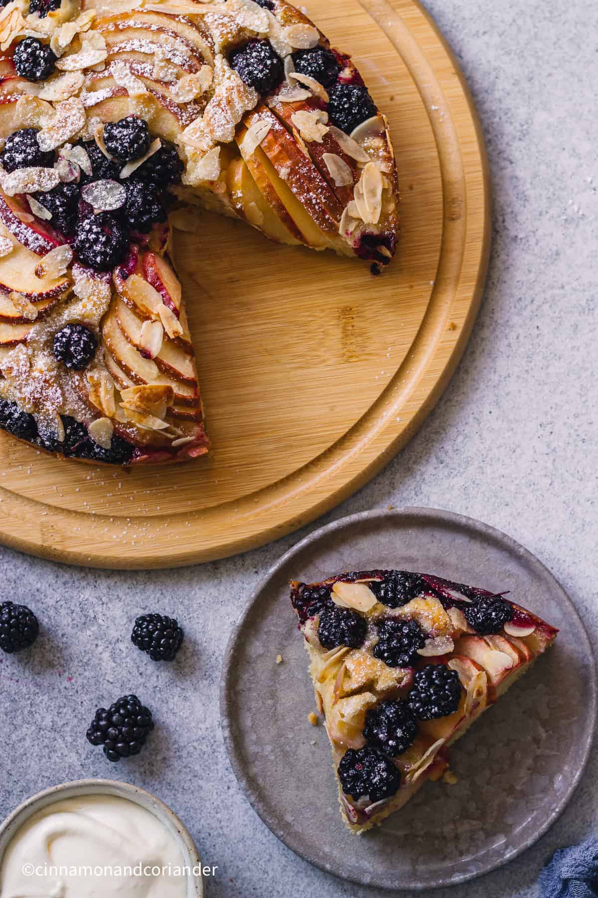 a slice of  Apple Blackberry Cake  next to the whole cake on a wooden cake platter