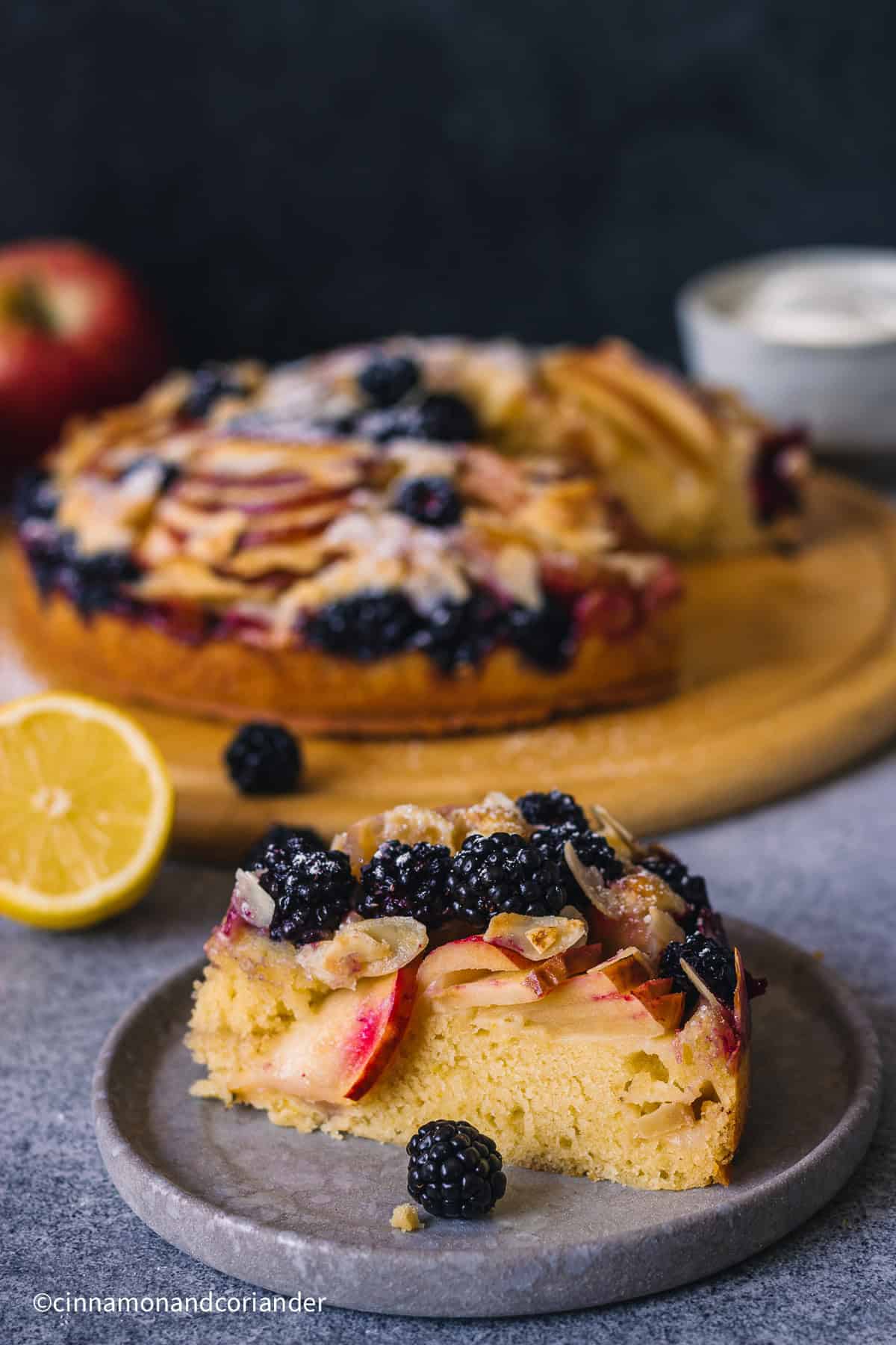 a slice of  Apple Blackberry Cake  on a stone plate decorated with fresh blackberries