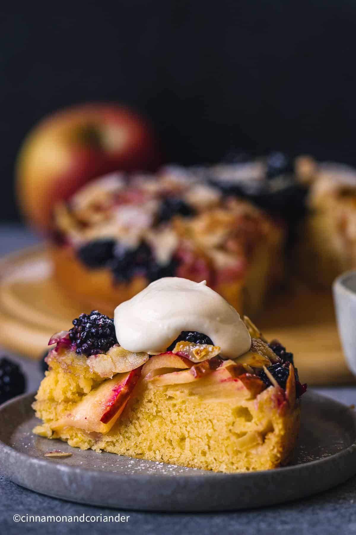a slice of rustic  Apple Blackberry Cake topped with a dollop of whipped cream