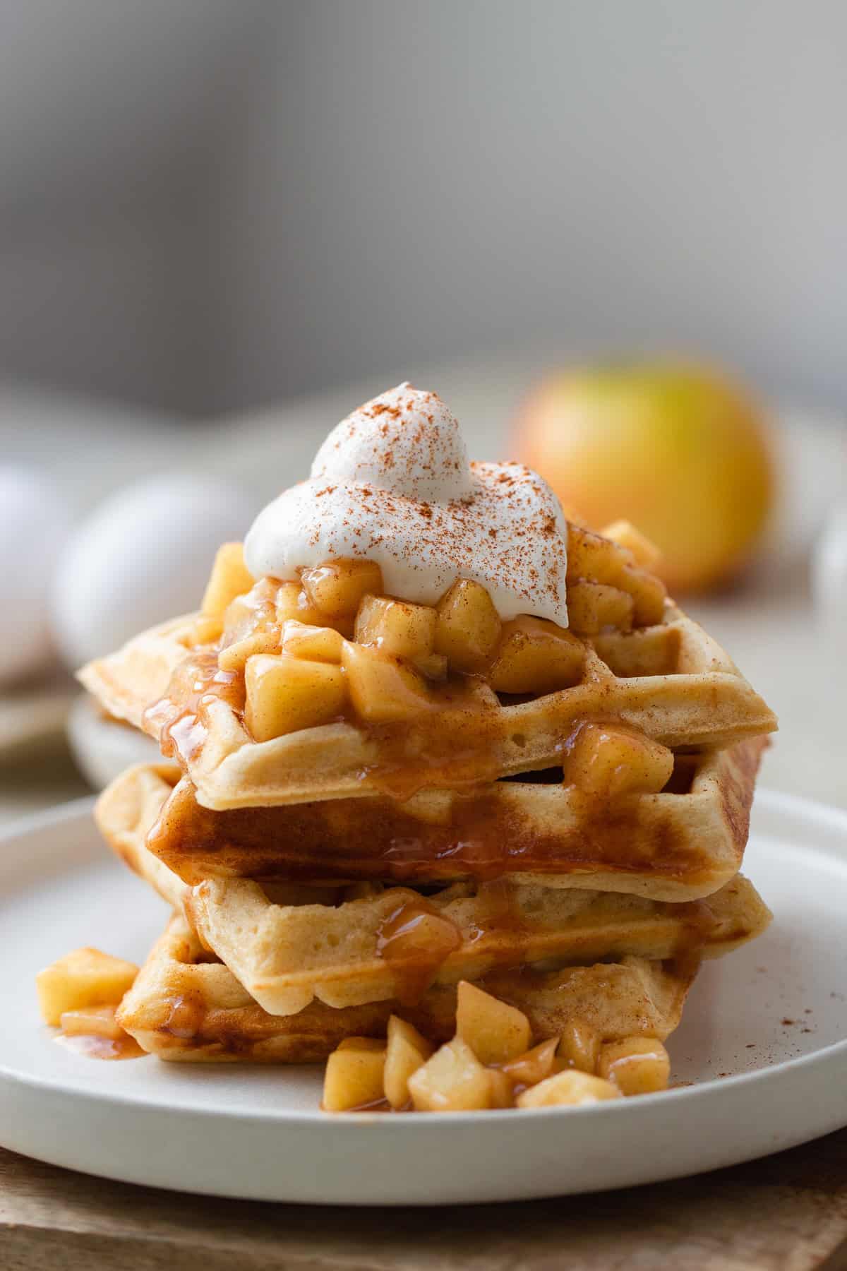 Nahaufnahme von einem Stapel Hefewaffeln mit Apfel Zimt Topping und Sahne serviert 
