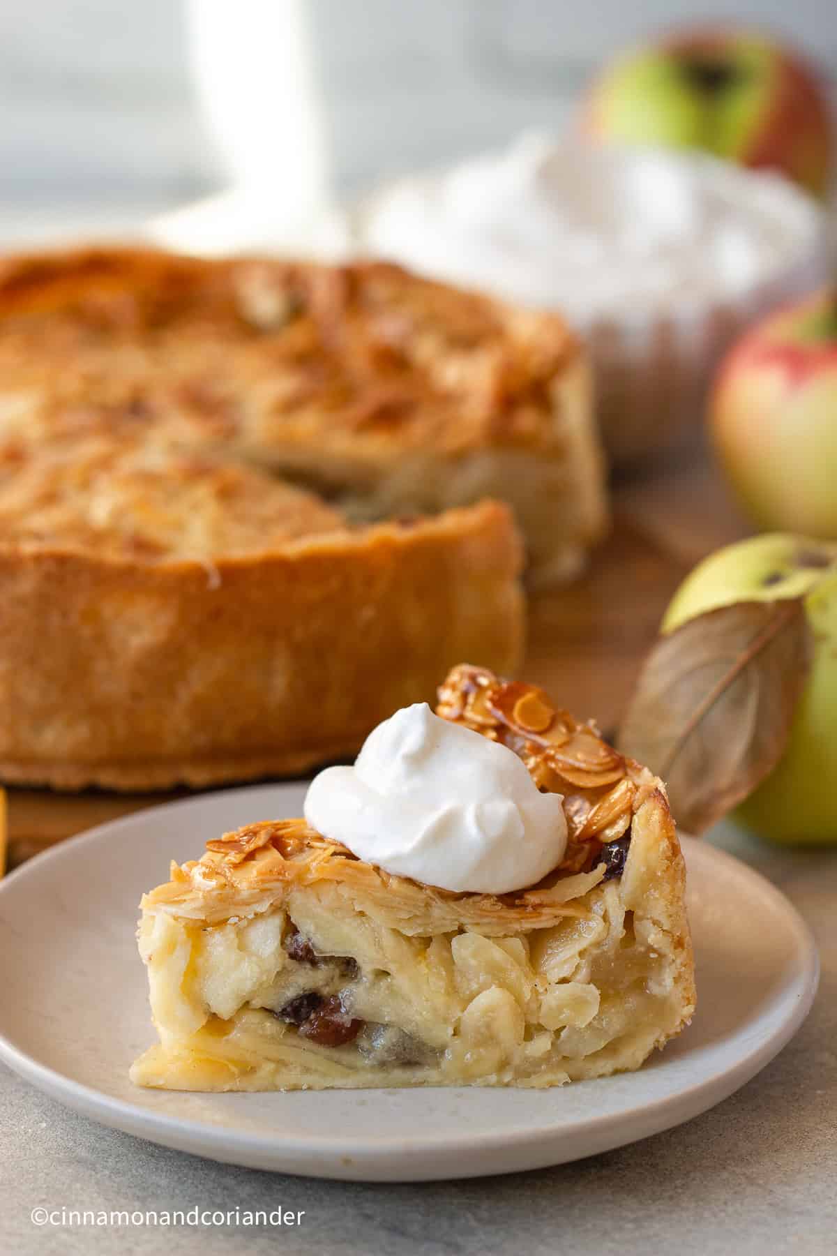 a slice of Florentine Apple Cake with almond topping served with whipped cream with fresh apples in the background