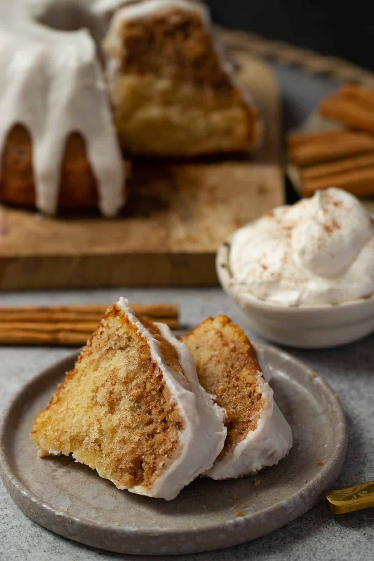 zwei Stücke Zimtschnecken Kuchen mit Zimt-Swirl, gerösteten Haselnüssen und Zuckerguss auf einem Dessert Teller mit einem Schälchen Sahne im Hintergrund