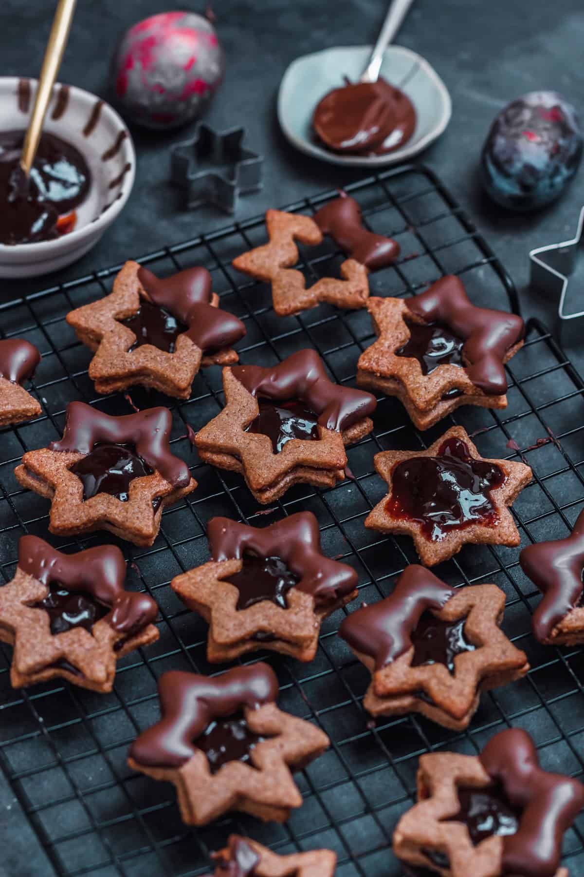 gefüllte Zimtsterne Plätzchen mit Pflaumenmus mit Schokoladen Glasur auf einem Gitter mit zwetschgen im Hintergrund 
